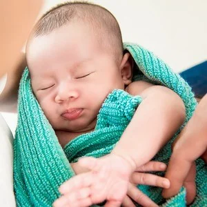 Bebê branco, enrolado em um pano verde.